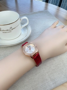 Detail of rose gold octagonal watch with diamond bezel and red leather strap on wrist
