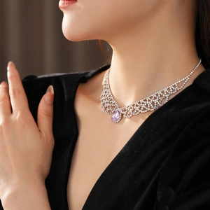 Dettaglio della collana in strass argentati con un ciondolo viola a goccia