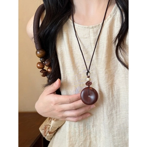 Primer plano de un colgante de madera tallada en un cordón de collar trenzado café
