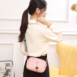 Pink woven crossbody camera bag with cat pendant and wide lettered shoulder strap