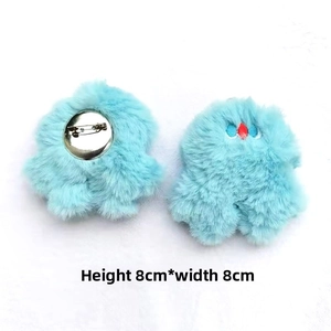 Front and back detail of a 8x8cm light blue plush monster brooch with embroidery