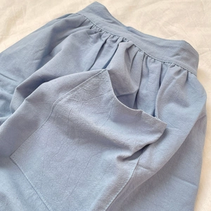 Macro detail of a light blue cotton apron featuring a large pocket and fine fabric texture
