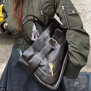 Deep brown leather tote bag with silver buckle and key charm shown in a street style look