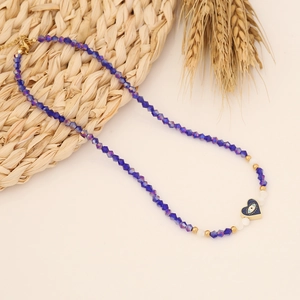 Dark blue beaded heart evil eye necklace with gold spacers on a natural straw mat