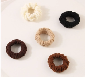 Detailed close-up of 5 elastic knit scrunchies in minimalist earth tones like beige and brown