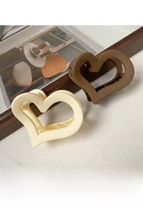 Detail view of hollow heart hair claws in matte beige and brown on white textured surface