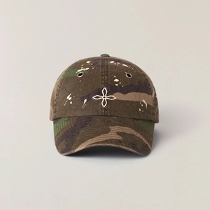 Detailed embroidery of white flower logo on vintage camo baseball cap with paint splatter