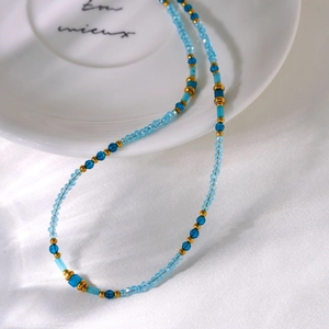 Blue beaded necklace with gold spacers elegantly draped on a white porcelain dish