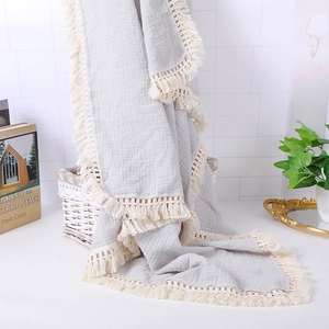 Detail of light grey muslin baby blanket featuring delicate cream tassel fringe edges