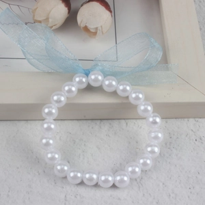 Close-up of a white imitation pearl bracelet with a light blue organza bow on wood background