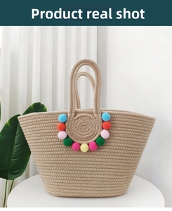 Detail of a beige straw tote bag featuring vibrant colorful pom-pom decorations on front