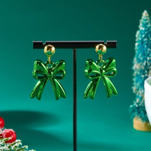 Close-up of green bow earrings with gold studs displayed on a festive Christmas setup
