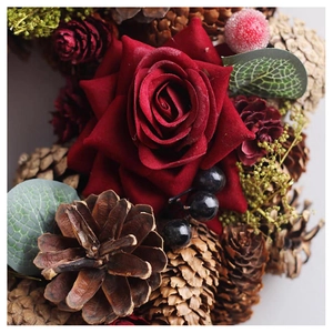 Close-up of velvet red rose, pine cones, and berries on a Christmas wreath ornament