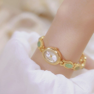 Detail of vintage gold chain watch with green stones and oval dial on female wrist