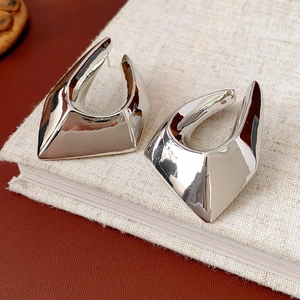 Macro shot of silver geometric metal earrings with a polished finish on a linen book