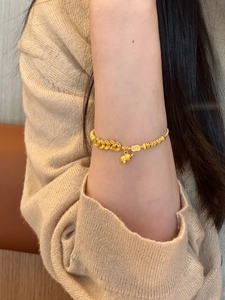 Close-up of a gold gourd charm bracelet with dual-texture chains on a model's wrist