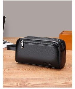 Close-up of black lychee grain leather men's clutch bag with metal zipper on a wooden desk