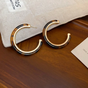 Detail of round C-shape earrings with gold metal and amber resin on wooden surface