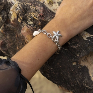 Silver stainless steel starfish and seashell pendant chain bracelet on a textured rock