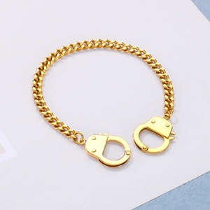 Close-up of golden Cuban link bracelet featuring detailed handcuff pendants in polished finish