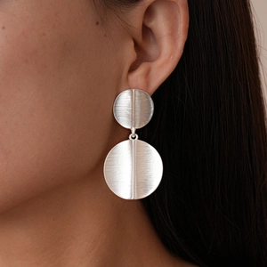 Close-up of geometric brushed silver round earrings on a model showing matte metal texture