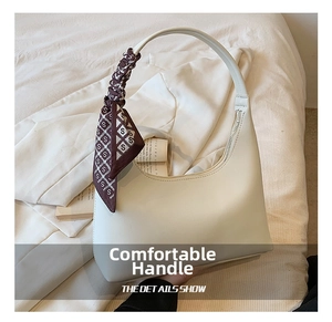 White leather underarm bag with decorative silk scarf handle on soft fabric background