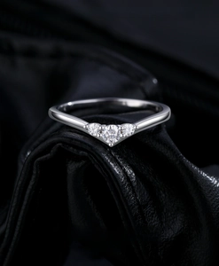 Macro shot of V-shaped silver ring with three brilliant diamonds on black leather texture