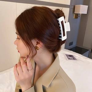 Gros plan d'une pince à cheveux géométrique blanche portée sur un chignon avec un blazer