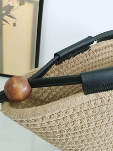 Minimalist beige woven tote bag with black leather handles and decorative wood beads