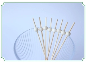 Bamboo fruit skewers with red wooden beads arranged in a clear glass on blue background