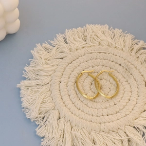 Detail of gold hoop earrings with spiral texture on a minimalist white backdrop