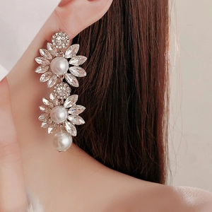Close-up of elegant flower earrings with sparkling crystals and white pearls on a model