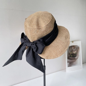 Cappello parasole in lino con grande fiocco nero su sfondo bianco minimalista