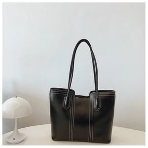 Detail of a black leather tote bag with contrast stitching on a minimalist table
