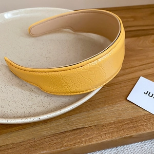 Detail of bright yellow pleated PU leather headband with non-slip lining on ceramic plate