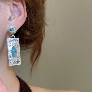 Detailed close-up of ethnic turquoise earrings with retro silver engraved patterns on a model