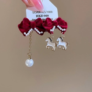 Détail de boucles d'oreilles nœuds en velours rouge avec perles et breloques poney