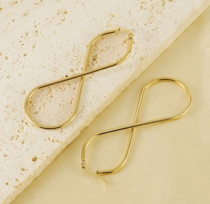 Détail de boucles d'oreilles infini en acier doré sur une plaque de pierre beige