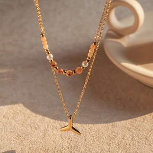 Detail of double-layer necklace with orange beads, pearls and golden fishtail pendant