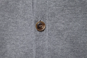 Macro shot of a textured brown button on a grey knitted business casual cardigan