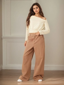 Top beige con hombros descubiertos y pantalones caqui de pierna ancha en modelo en cuarto minimalista