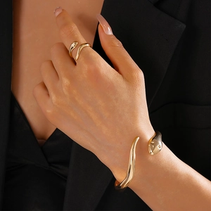 Detail of minimalist gold snake-shaped open bracelet and ring set on model