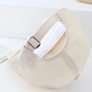 Close-up of the adjustable metal buckle on back of the beige cotton baseball cap