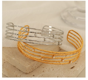 Detail of multi-layer C-shape bangles with hammered metal texture and pearl accents