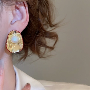 Close-up of elegant gold petal earrings with pearl and red trim on a female model