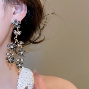 Macro view of gold flower tassel earrings with dark grey and clear rhinestones on model