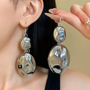 Close-up of oversized irregular silver metallic drop earrings on a model with clean lighting