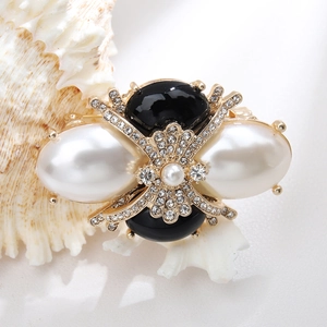 Detailed close-up of golden brooch with black gems and white imitation pearls