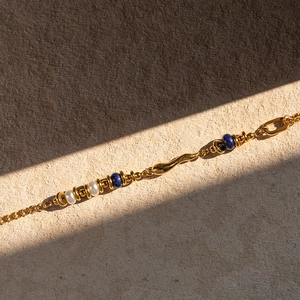 Detailed shot of 18k gold plated bracelet featuring white pearls and blue beads on sand background