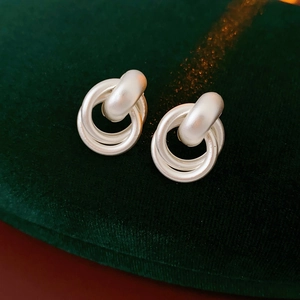 Close-up of interlocking matte silver hoop earrings on a dark green velvet stand